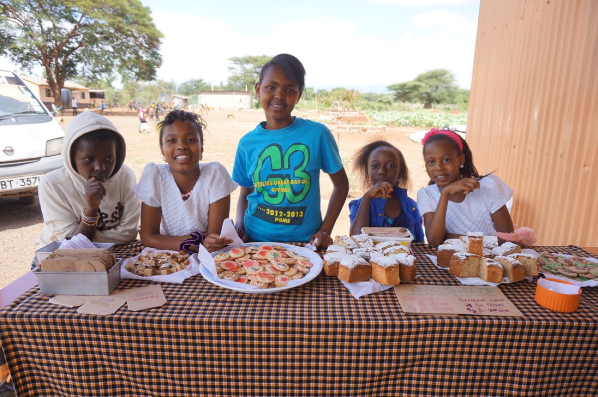 Five pupils stand behind a table of cookies and cake at the school bake sale.