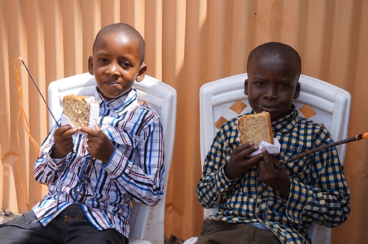 Two boys sit on white chairs, each holding a slice of banana cake.